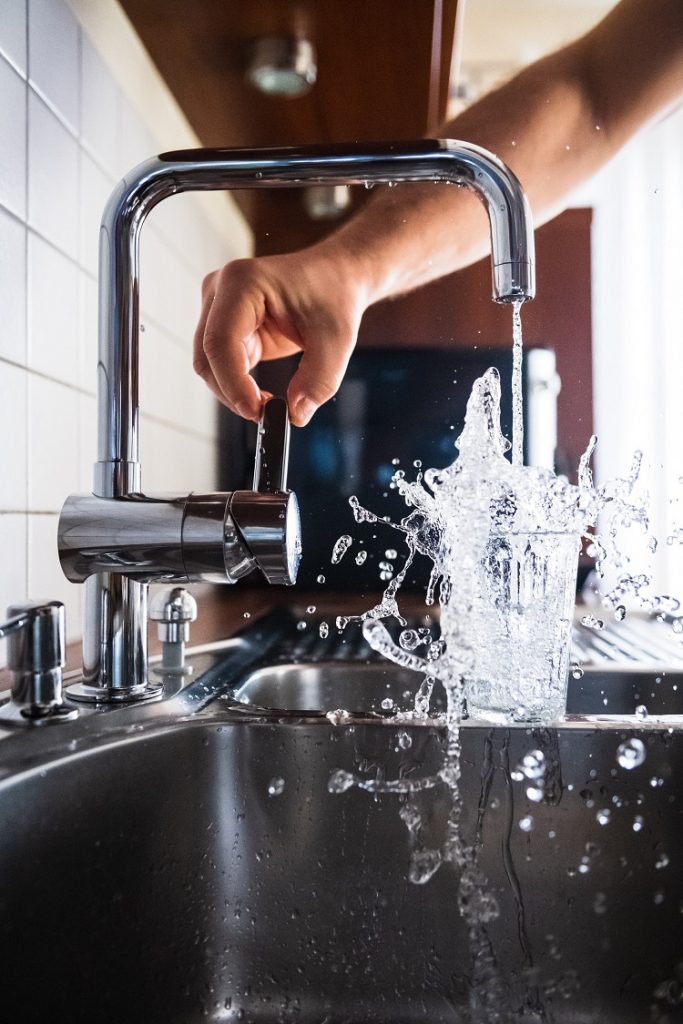 picture of kitchen sink with a glass in it  and a tap with a big splash of water